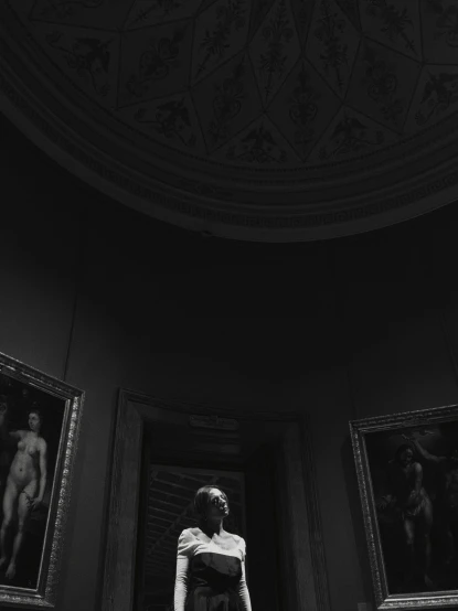 a woman standing in a room with paintings on the wall, a black and white photo, inspired by Antonio Canova, unsplash contest winner, museum diffuse lighting, photography alexey kurylev, summer evening, rotunda