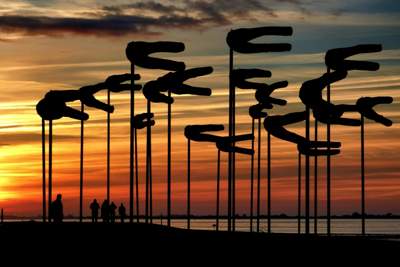 a group of flags sitting on top of a beach, an abstract sculpture, by Jan Tengnagel, pexels contest winner, kinetic art, silhouette over sunset, serpentine maze, tubes, 5 feet away