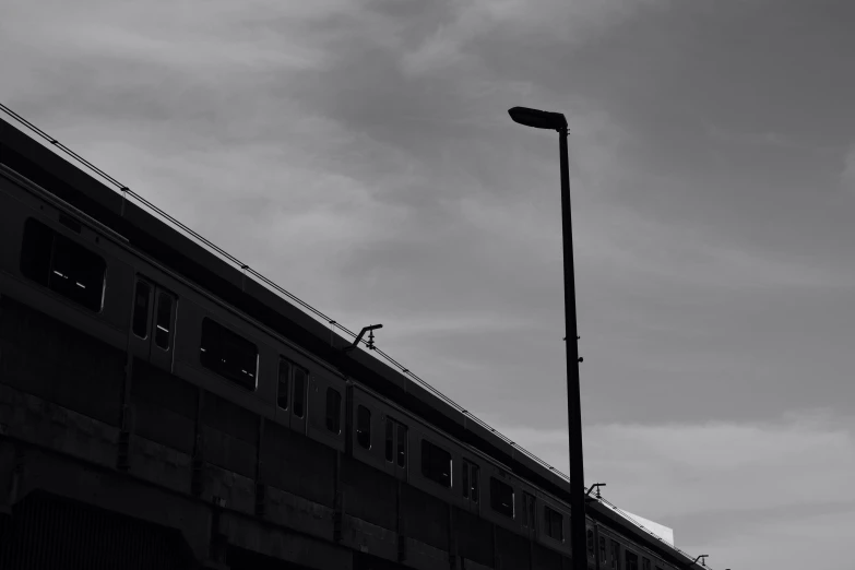 a black and white photo of a train going over a bridge, postminimalism, under street lamp, silhouette :7, bus station, desolate :: long shot