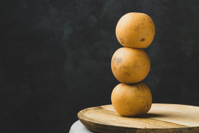 a stack of three oranges sitting on top of a wooden plate, inspired by Kanō Naizen, unsplash, process art, north island brown kiwi, dough sculpture, high resolution product photo, made of cheese