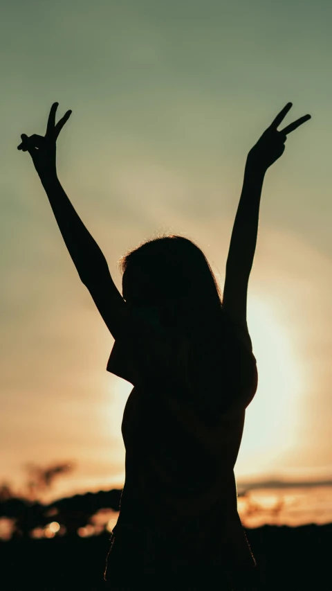 a silhouette of a woman with her hands in the air, an album cover, pexels contest winner, bare shoulders, golden hour 8k, grainy photo, pose(arms up + happy)