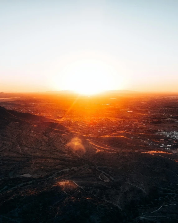 the sun sets over a mountain range with a plane in the sky