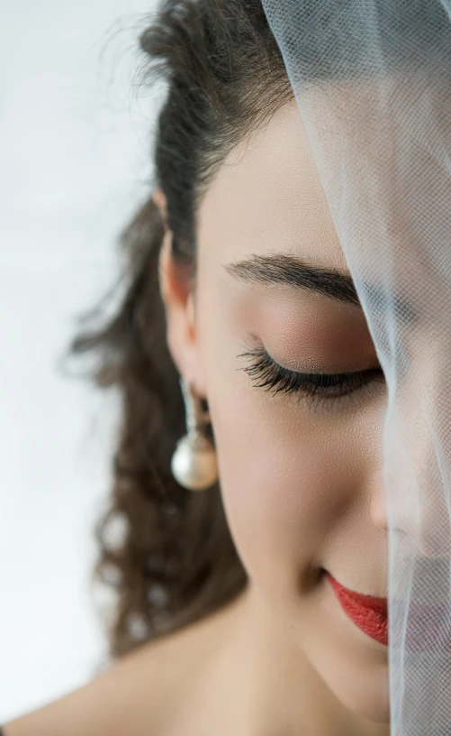 a close up of a woman wearing a veil, eyes half closed, mascara, earring, bride