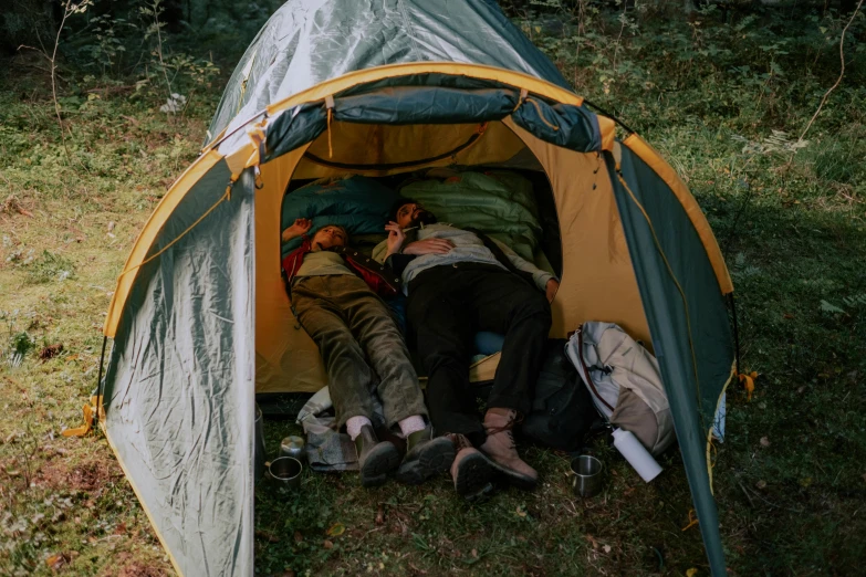 a couple of people laying inside of a tent, by Jessie Algie, pexels contest winner, hiking clothes, yellow and charcoal leather, asleep, people resting on the grass