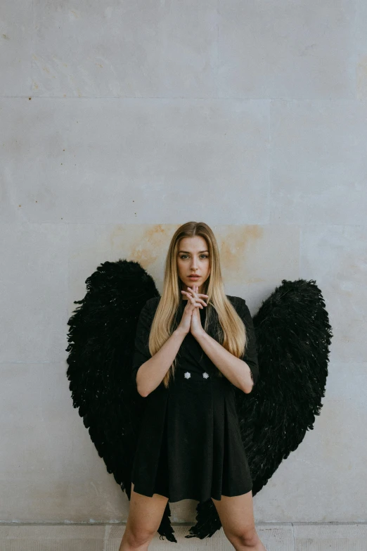 a woman standing in front of a wall with black wings, by Marie Angel, pexels contest winner, anya taylor joy, religious, raphael personnaz, large)}]