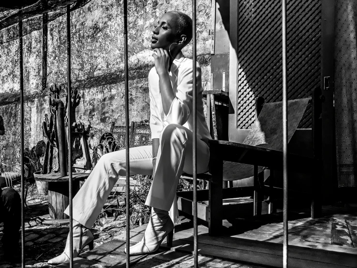 a black and white photo of a man sitting in a cage, by Daniel Gelon, a beautiful woman in white, in style of nadine ijewere, white pants, in the sun