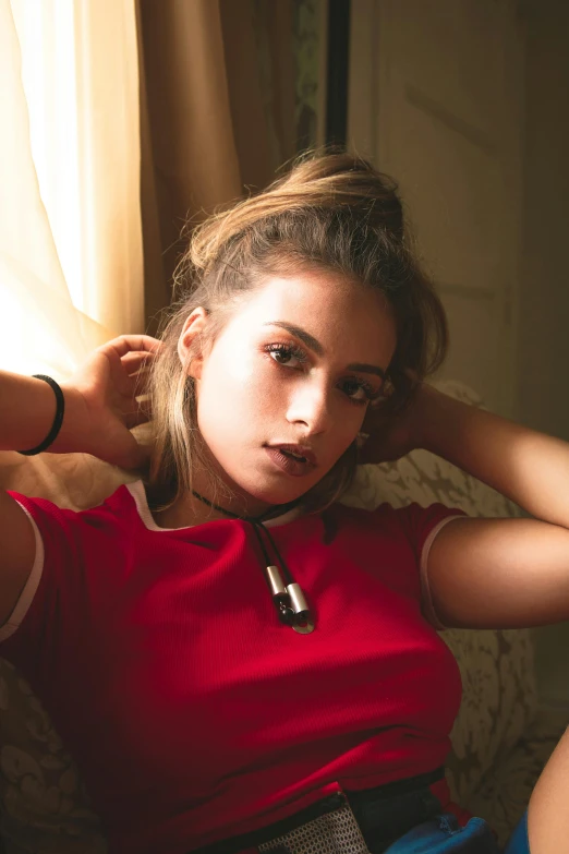 a woman sitting on top of a couch next to a window, a portrait, inspired by Elsa Bleda, trending on pexels, light stubble with red shirt, earbuds jewelry, attractive girl tomboy, wearing choker