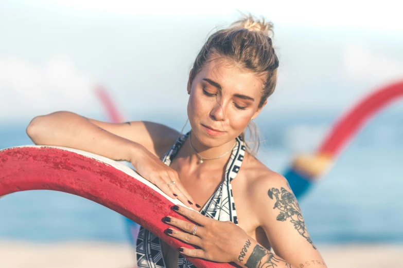 a woman standing on top of a beach holding a surfboard, pexels contest winner, happening, blue and red tattoo, avatar image, close up portrait photo, sitting down