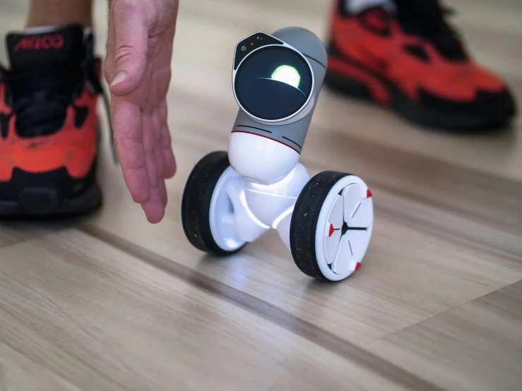 a small robot sitting on top of a wooden floor, silver white red details, twirly, formula 1, press shot