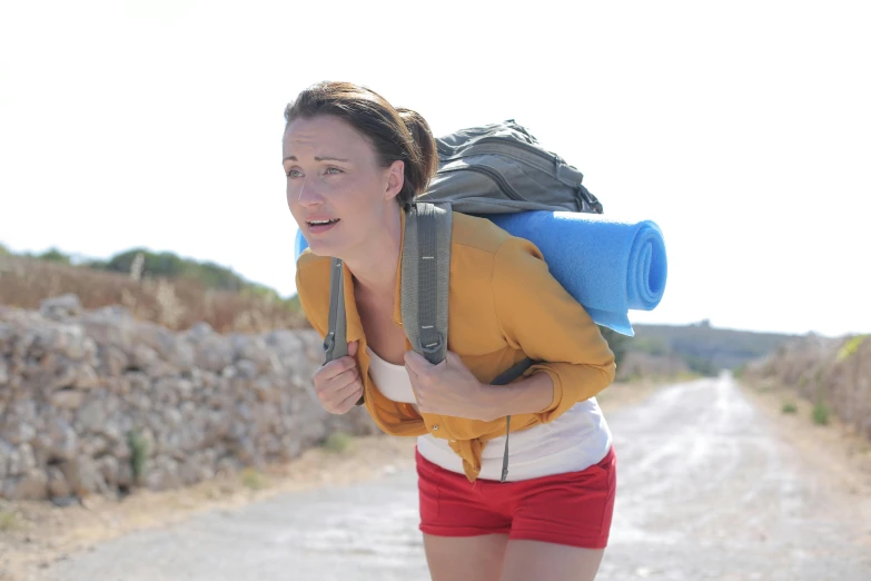 a woman with a backpack walking down a dirt road, a picture, wearing a vest top, parody, filmstill, sweating