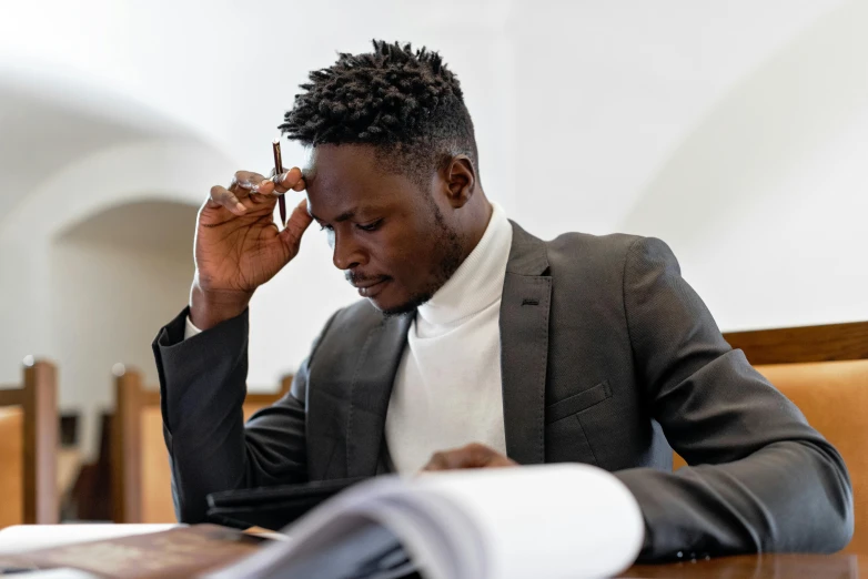 a man sitting at a table with a pen in his hand, an album cover, pexels contest winner, academic art, stressed expression, african man, lawyer, showing forehead