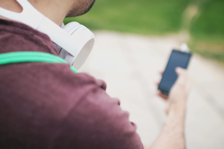 a close up of a person holding a cell phone, by Dan Content, trending on pexels, headphones on his head, at a park, mobile learning app prototype, haze over the shoulder shot