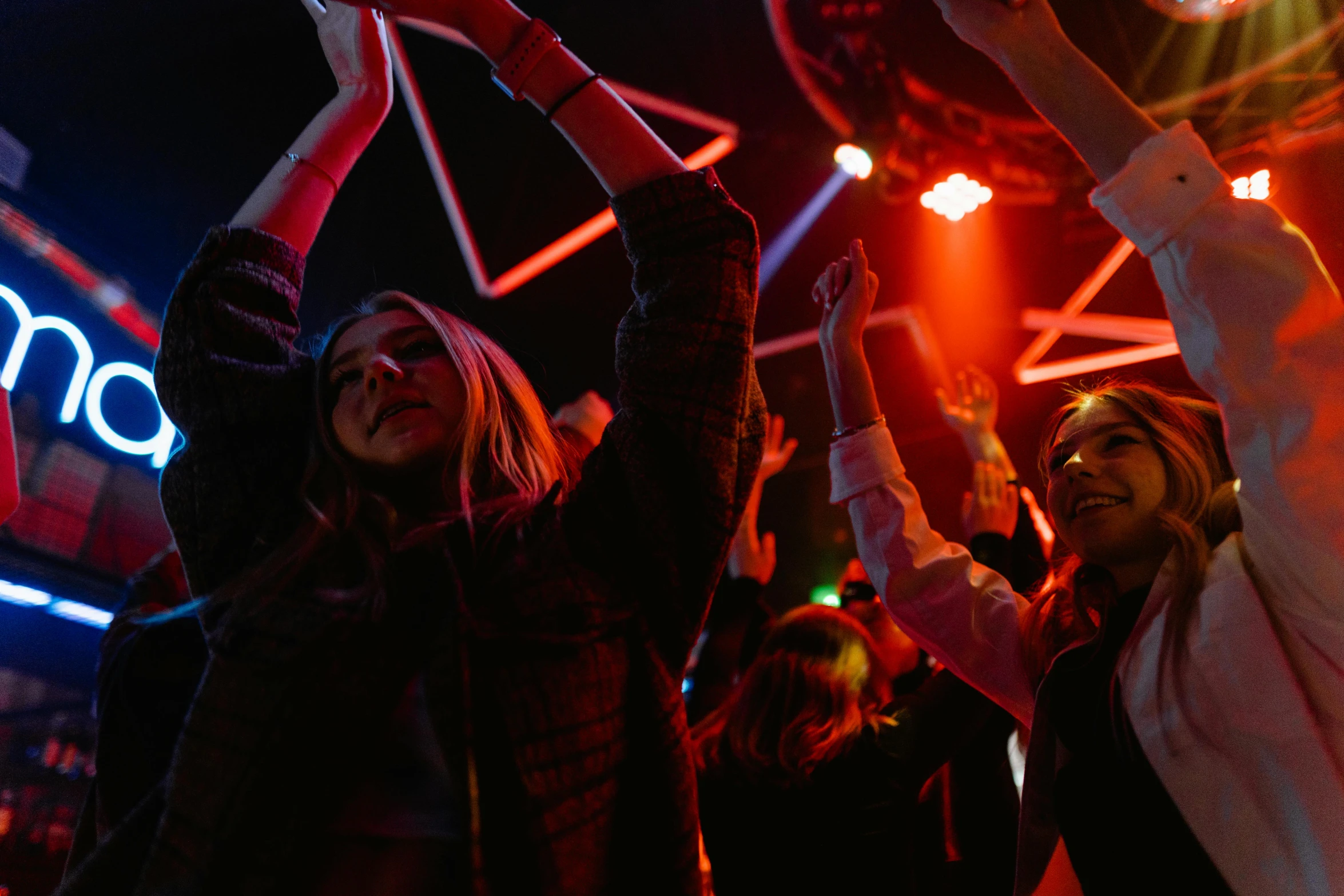 a group of people standing in front of a neon sign, pexels, happening, dancefloor, with arms up, red light, photograph of three ravers