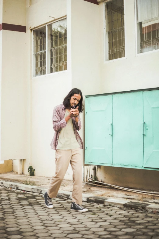 a man walking down a cobblestone street talking on a cell phone, by Basuki Abdullah, trending on unsplash, pastel clothing, leaning on door, mid long hair, indonesia