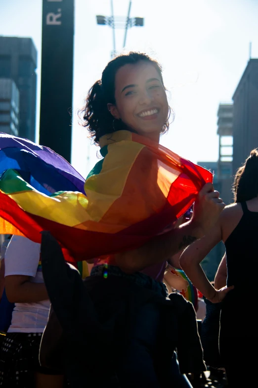 a woman holding a rainbow flag in a crowd, a photo, slide show, taken at golden hour, smiling, blanca alvarez