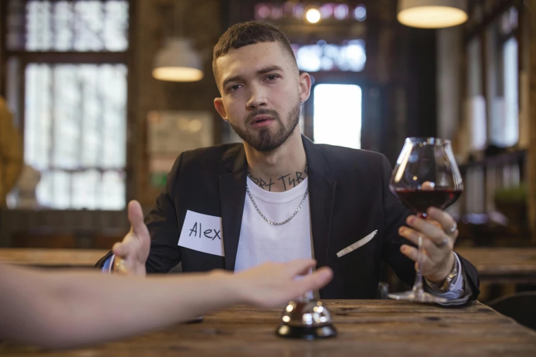 a man sitting at a table with a glass of wine, inspired by Dan Smith, tattooed, looking straight to camera, artem, commercial