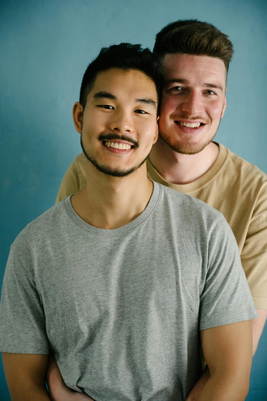 two men pose for the camera in front of a blue wall