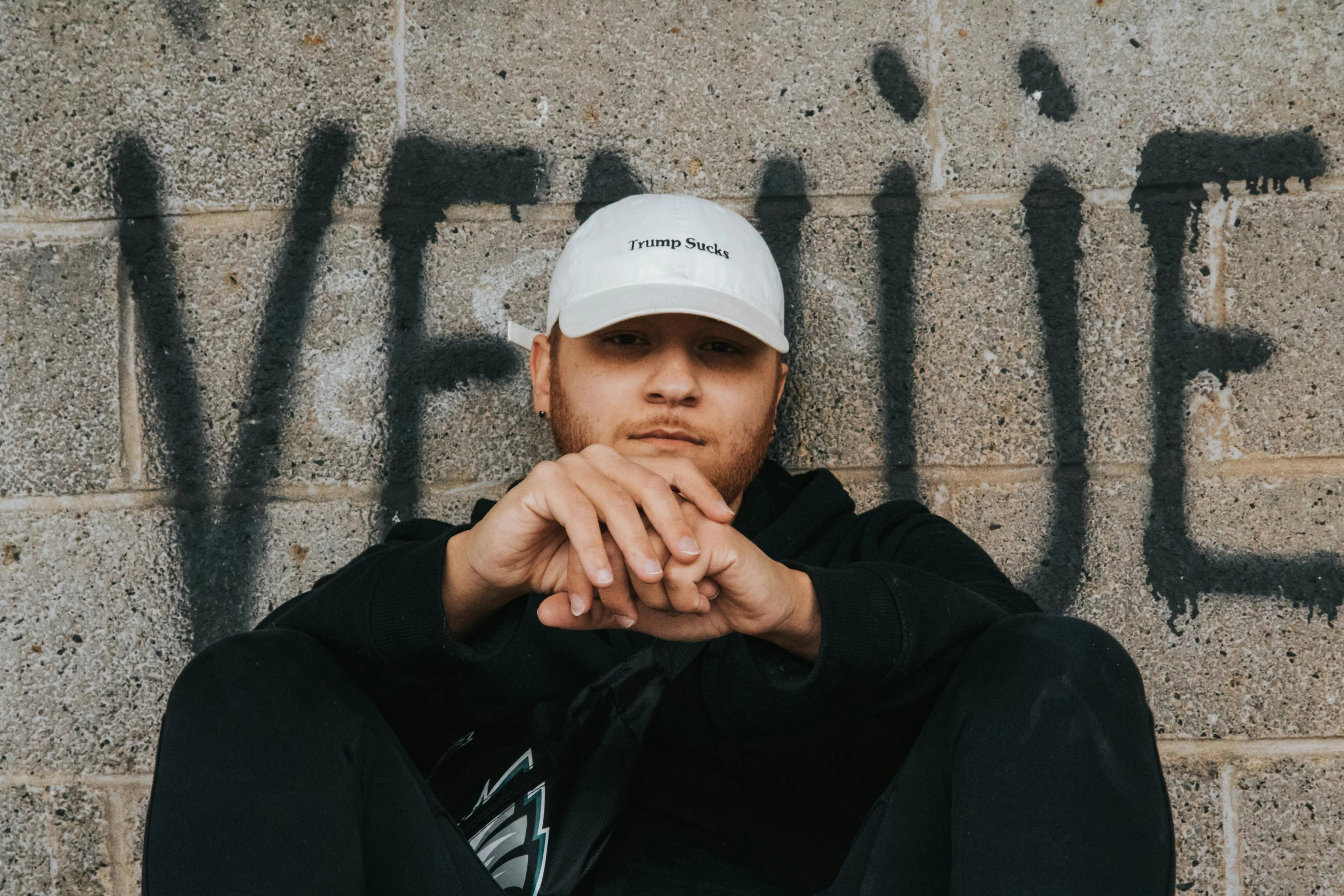 a man wearing a white hat is standing next to a wall with graffiti