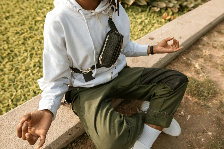 a man with dreadlocks sitting on a curb, by Nina Hamnett, trending on pexels, happening, wearing an ammo belt, white and black clothing, bag over the waist, green and brown clothes
