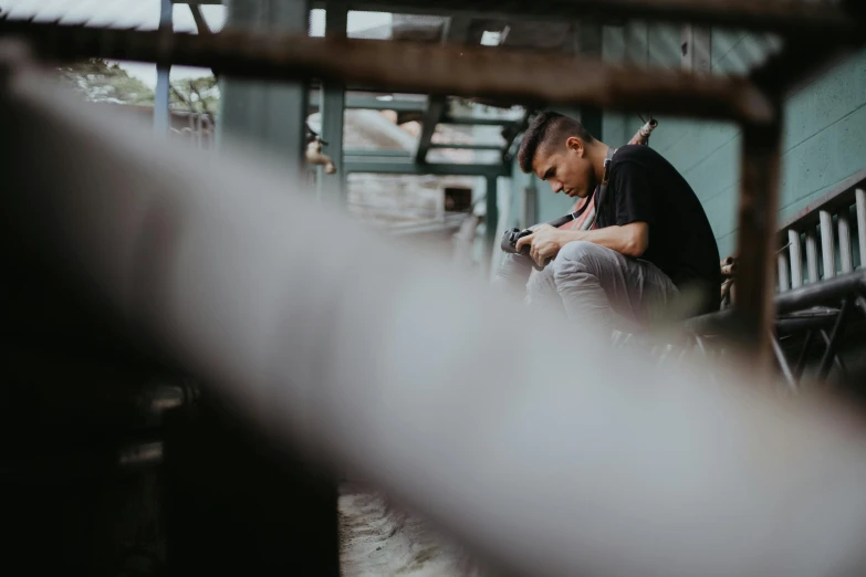 a man sitting on a bench looking at his cell phone, a picture, pexels contest winner, in a factory, male teenager, faded and dusty, portrait featured on unsplash