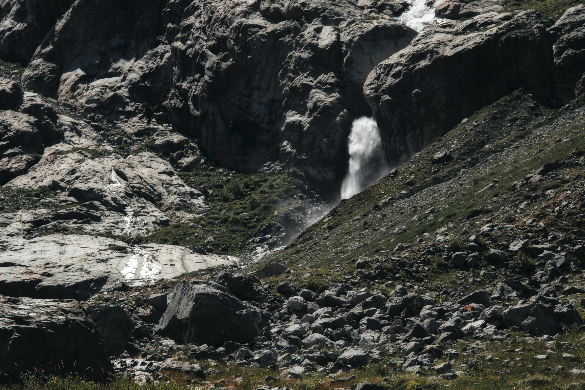 a couple of sheep walking through the mountains with a waterfall behind them