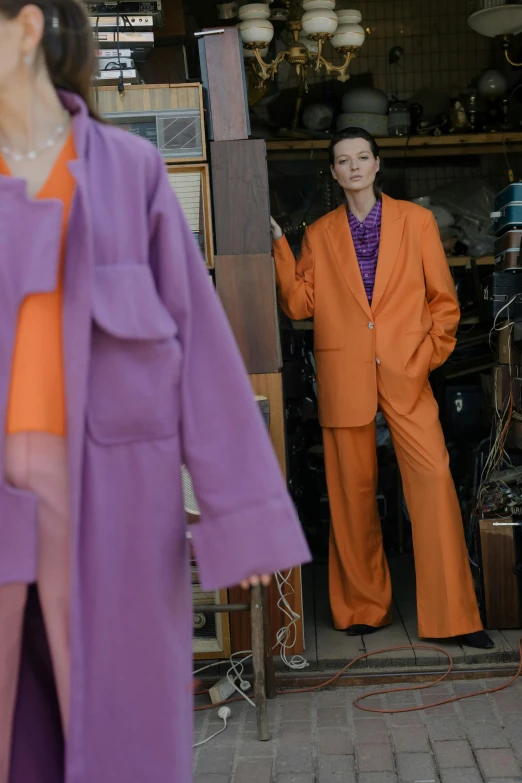 a woman in a purple coat and orange pants, by Caro Niederer, trending on pexels, bauhaus, tilda swinton, met collection, discarded mechsuit in background, tokio