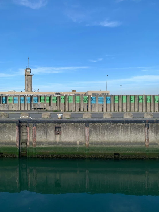 a train sitting on top of a train track next to a body of water, concrete building, banner, blue and green water, concrete pillars