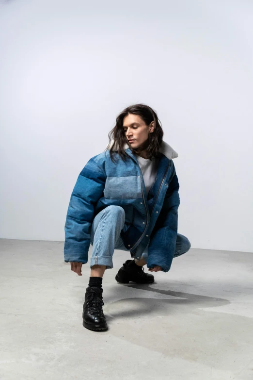 a woman is squatting down on the floor wearing a blue coat