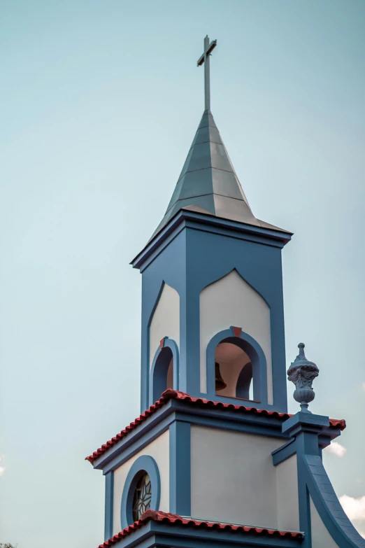 a blue and white church tower with a cross on top, inspired by Pedro Álvarez Castelló, red roofs, são paulo, up-close, lead - covered spire