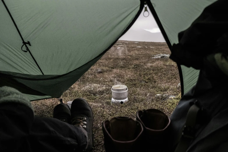 a couple of people sitting inside of a tent, by Else Alfelt, pexels contest winner, hurufiyya, table in front with a cup, highlands, wet ground, about to step on you