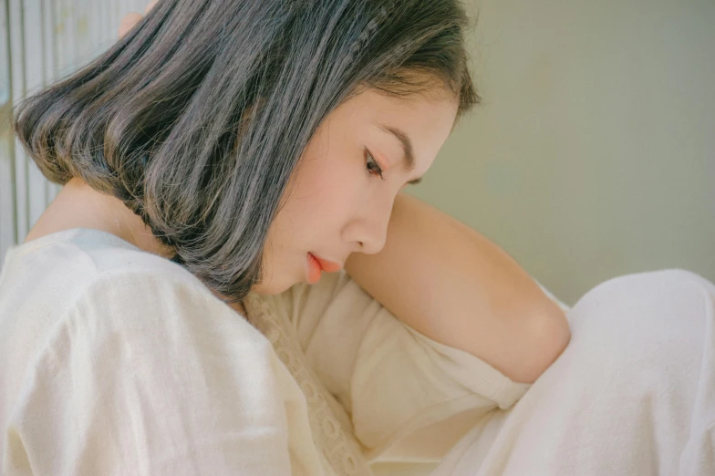 a woman sitting on top of a bed next to a window, by Ye Xin, trending on pexels, pouty lips, looking her shoulder, tired half closed, colored