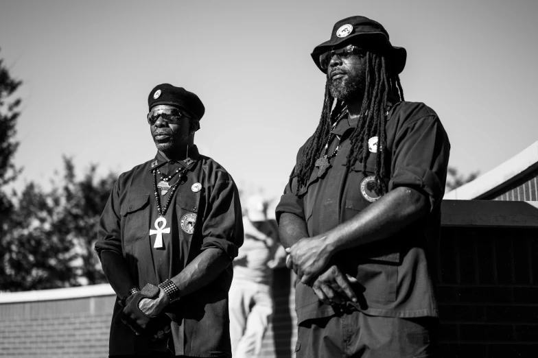 a couple of men standing next to each other, a black and white photo, by Dan Frazier, unsplash, black arts movement, in black uniform, george clinton, battle ready, wearing chains