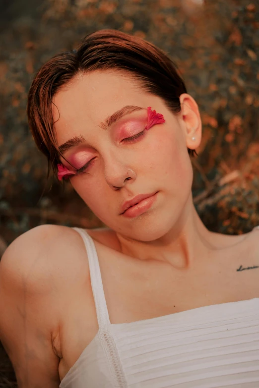 a woman laying on the ground with her eyes closed, an album cover, inspired by Elsa Bleda, trending on pexels, pastel makeup, portrait androgynous girl, red left eye, pink petals