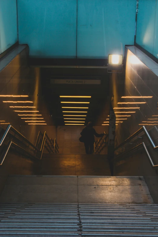 a person standing at the bottom of an escalator, inspired by Elsa Bleda, light and space, yellow street lights, steps leading down, train station, unsplash photography