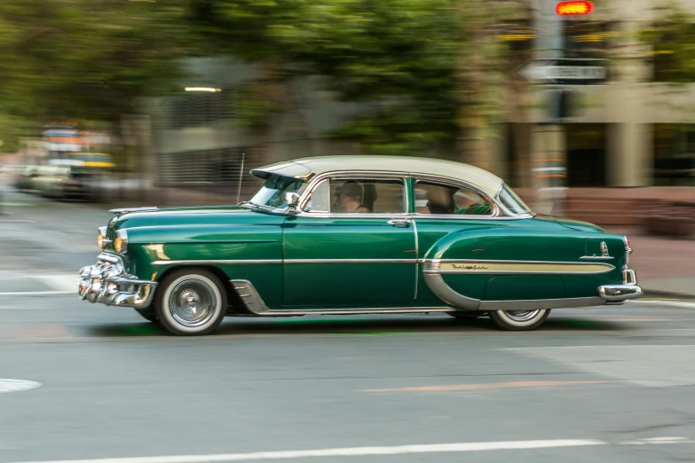 a green car driving down a street next to a traffic light, by Dave Melvin, pexels contest winner, 1957 chevrolet bel air, melbourne, panning shot, profile image