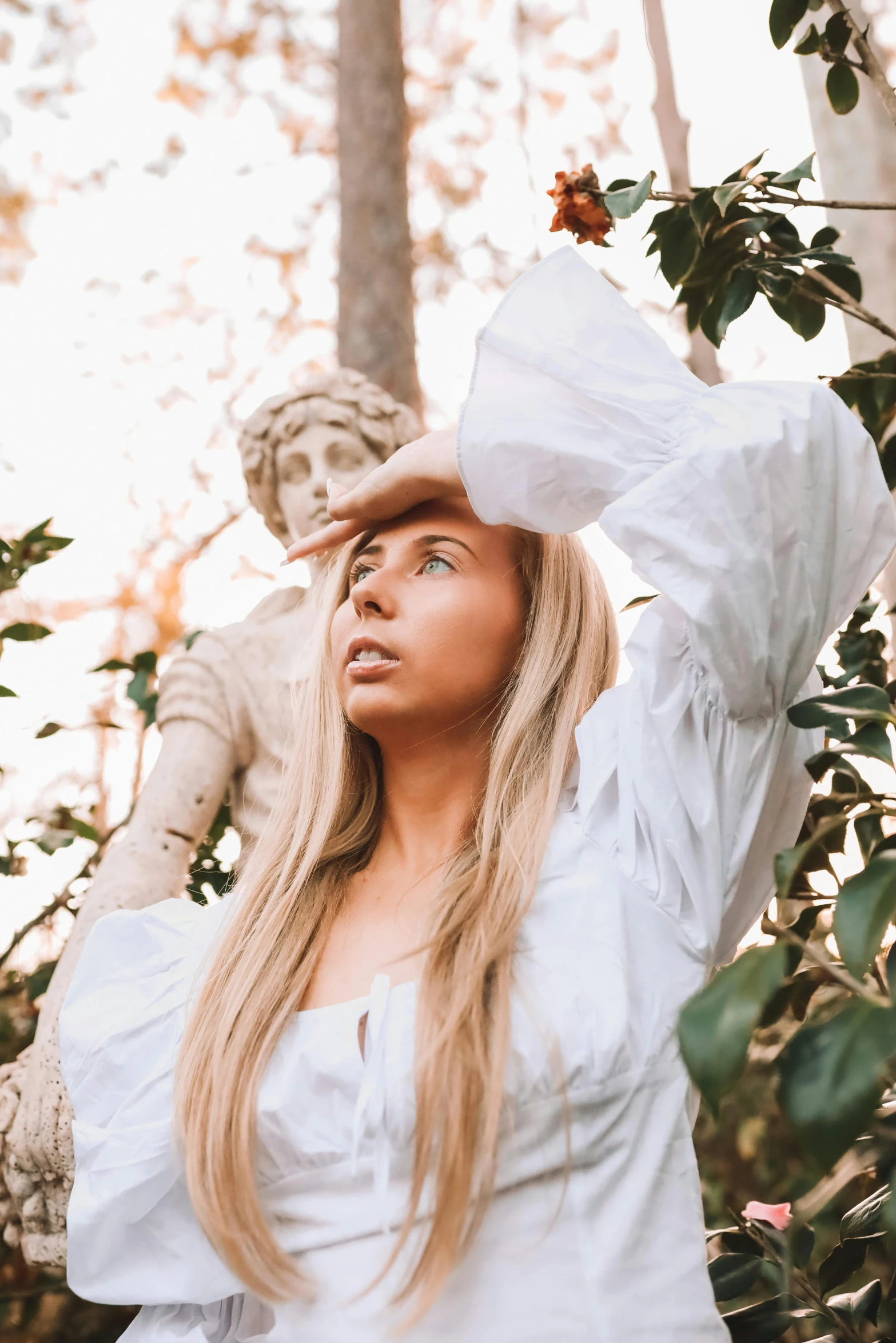 a woman standing next to a statue in a forest, an album cover, unsplash contest winner, renaissance, silken blonde hair, clothed in white shirt, portrait of vanessa morgan, looking at the sky