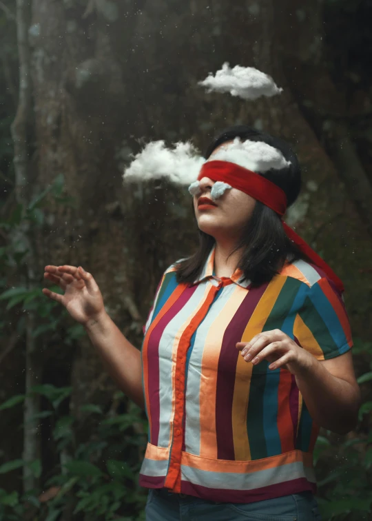 a woman wearing colorful clothes standing in the forest with her hand out