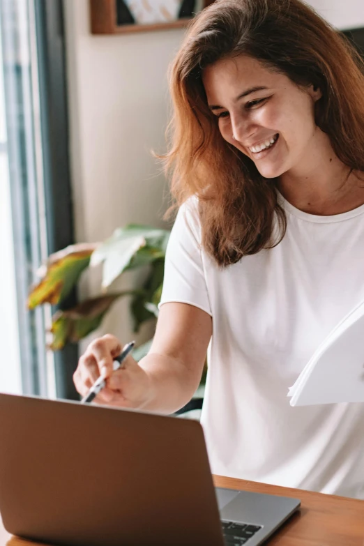 a woman sitting at a table working on a laptop, pexels contest winner, happening, earing a shirt laughing, holding a clipboard, drawing on a parchment, banner