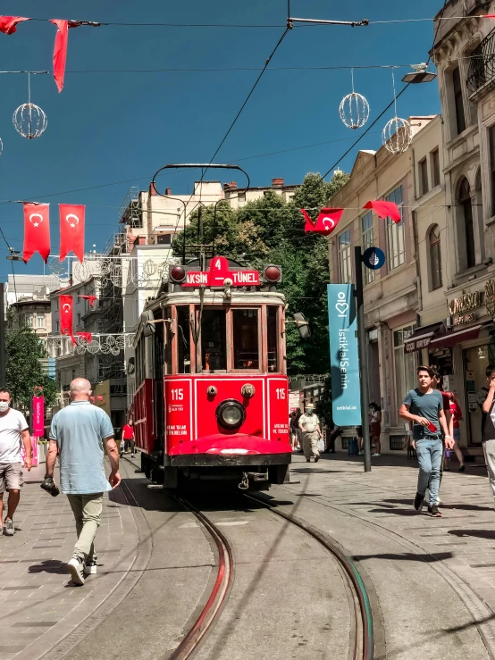 a red trolly travels on the street while people walk by