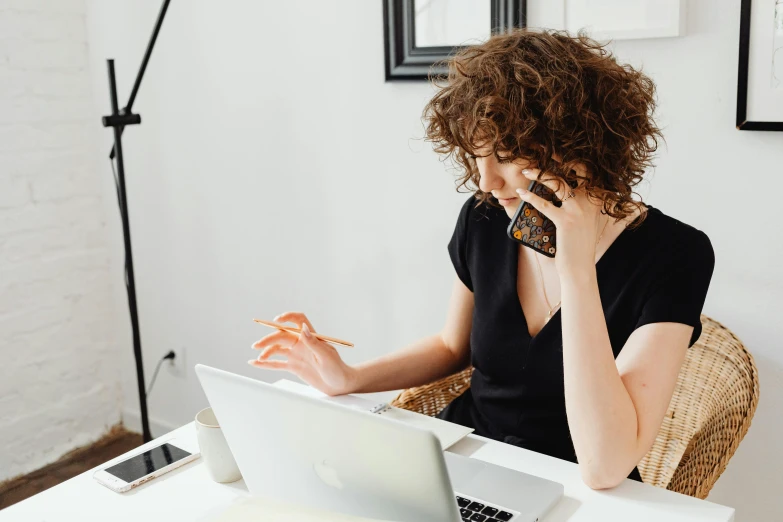 a woman sitting at a table talking on a cell phone, trending on pexels, working on a laptop at a desk, curly haired, d&d boss, slightly minimal