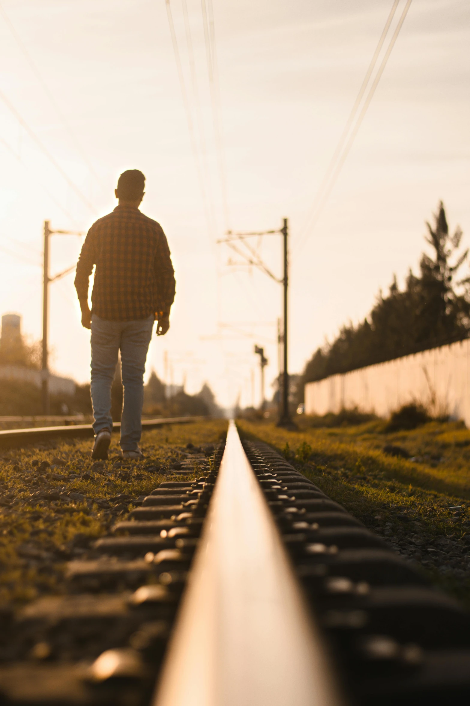 a man walking down a train track at sunset, by Niko Henrichon, unsplash, full body profile, neighborhood, head turned, over - detailed