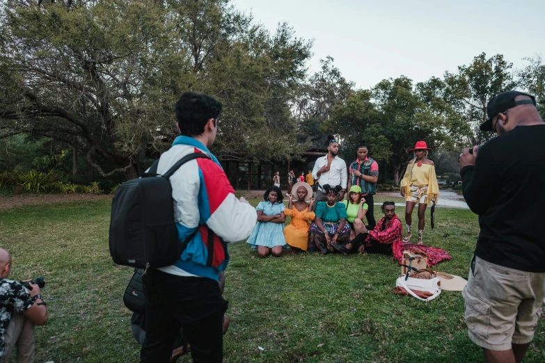 a group of people sitting on top of a lush green field, a portrait, by Lee Loughridge, pexels contest winner, hurufiyya, cardistry, giving a speech, aboriginal australian hipster, giving gifts to people