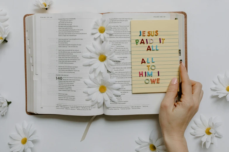 a woman's hand holding a notepad with the words jesus, faith, all to him, and love written on it, pexels contest winner, analytical art, books and flowers, thumbnail, paper cut out, 1 2 9 7