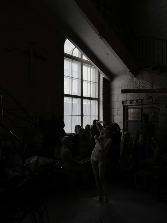 a woman standing in front of a window in a dark room, a statue, inspired by Vanessa Beecroft, pexels contest winner, soviet yard, group of people in a dark room, inside a warehouse, taken in the late 2010s