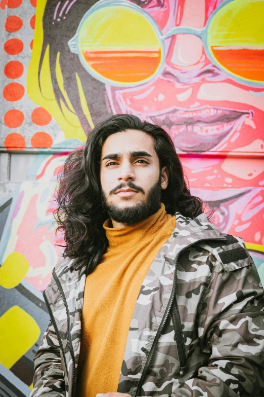 a man standing in front of a graffiti wall, an album cover, inspired by Ismail Acar, trending on pexels, mid long hair, headshot profile picture, lgbtq, man wearing a closed cowl