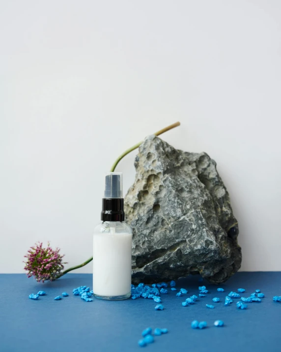 a bottle of body lotion next to a rock, inspired by Marina Abramović, unsplash, jpeg artefacts on canvas, thumbnail, manicured, miniature product photo