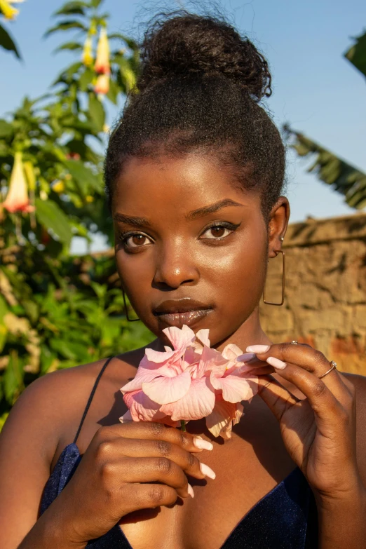 a woman holding a flower in front of her face, by Lily Delissa Joseph, photoshoot for skincare brand, ( ( dark skin ) ), sunbathed skin, pink