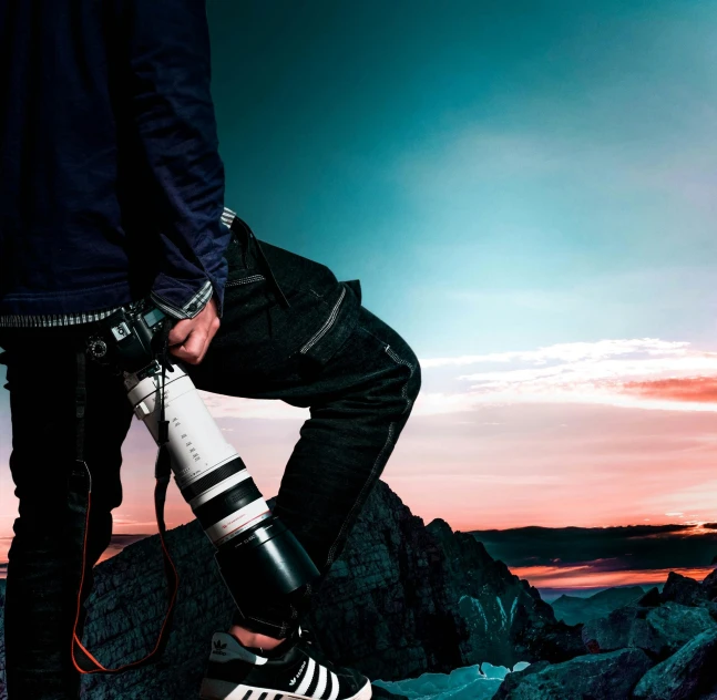 a man holding a camera on top of a rock, an album cover, by Jesper Knudsen, pexels contest winner, prosthetic leg, wearing space techwear, with sunset, sneaker photo