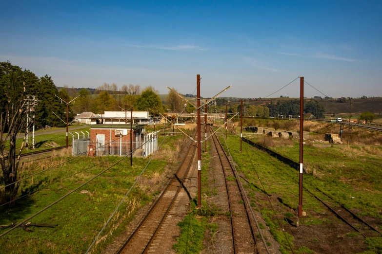 a train traveling down train tracks next to a lush green field, telephone wires, liege, 2022 photograph, industrial buildings