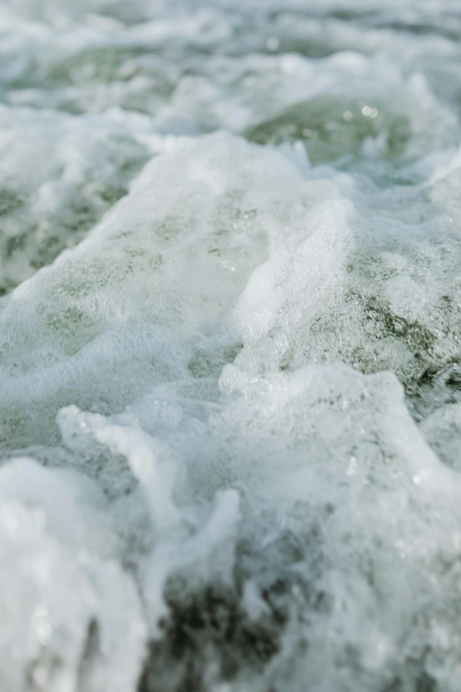 a person riding a surfboard on a wave in the ocean, moist mossy white stones, covered in ice, zoomed in, fluids